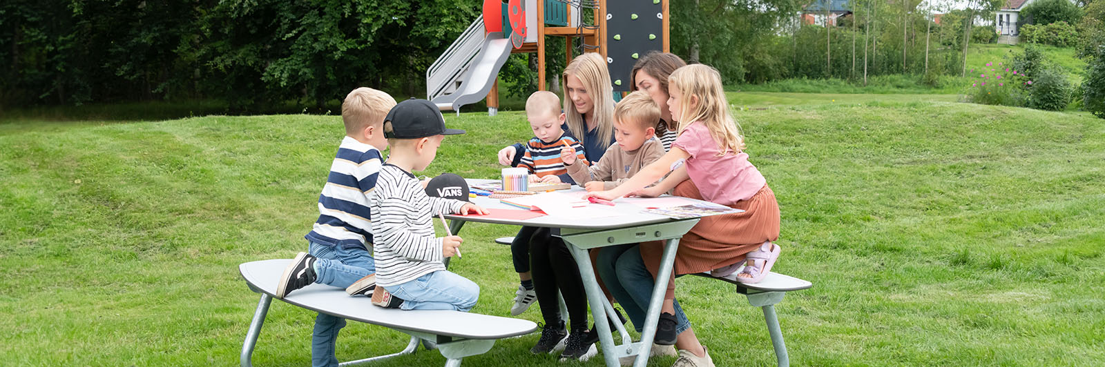 Gran mesa de picnic HPL, está llena de adultos y niños, están dibujando y charlando. 